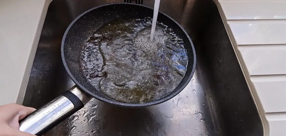 frying pan with non-stick surface and hot oil under water tap flow in sink