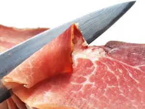 A chef's knife slicing ham