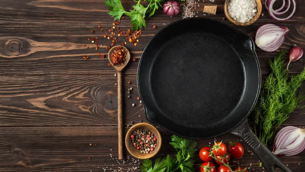 herbs and spices around cast iron skillet on wooden background