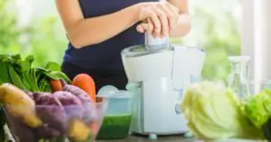 woman making smoothie with fresh vegetables in the blender in kitchen at home